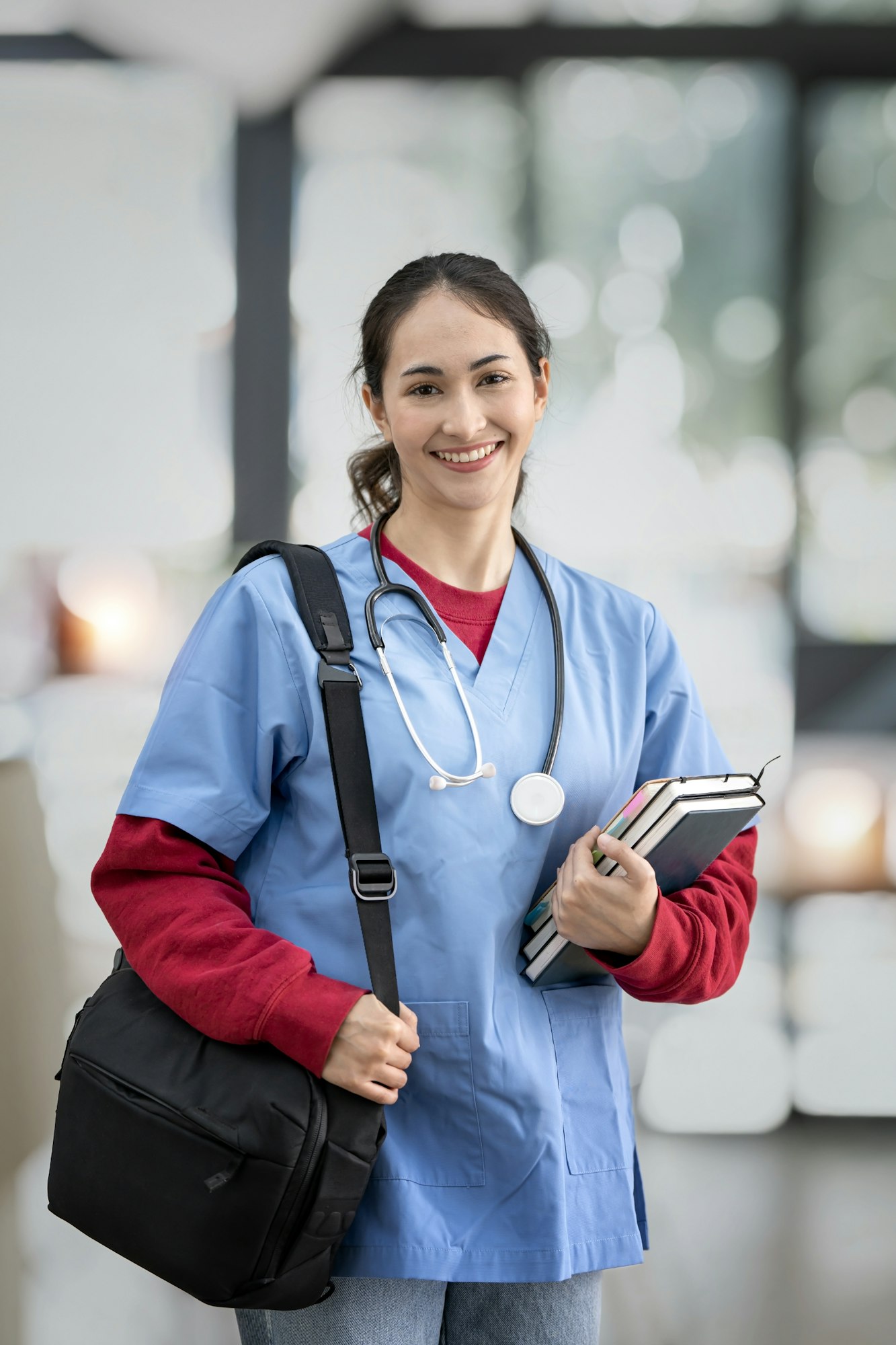 Young female doctor or nurse, nurse student or intern holding book and bag standing